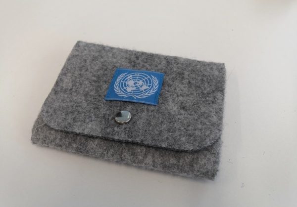 Vaaleanharmaa huovasta tehty rahakukkaro, jonka kannessa metallinen avattava neppari. Kanteen ommeltu kankainen neliö, jossa sinisellä pohjalla YK:n logo